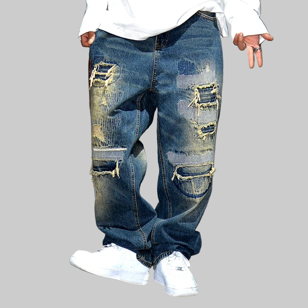 VOIDWEAR VDR_VANISH_05 ☰ baggy ripped patch jeans with distress wash, hip hop fit, ritual-coded glyph embroidery. Ripped blue jeans worn by a person on a gray background