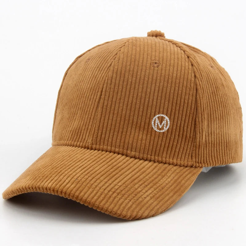 Diamond-studded M-letter corduroy baseball cap in solid color with adjustable strap, unisex streetwear headwear by VOIDWEAR.. Brown corduroy cap with a logo on a white background