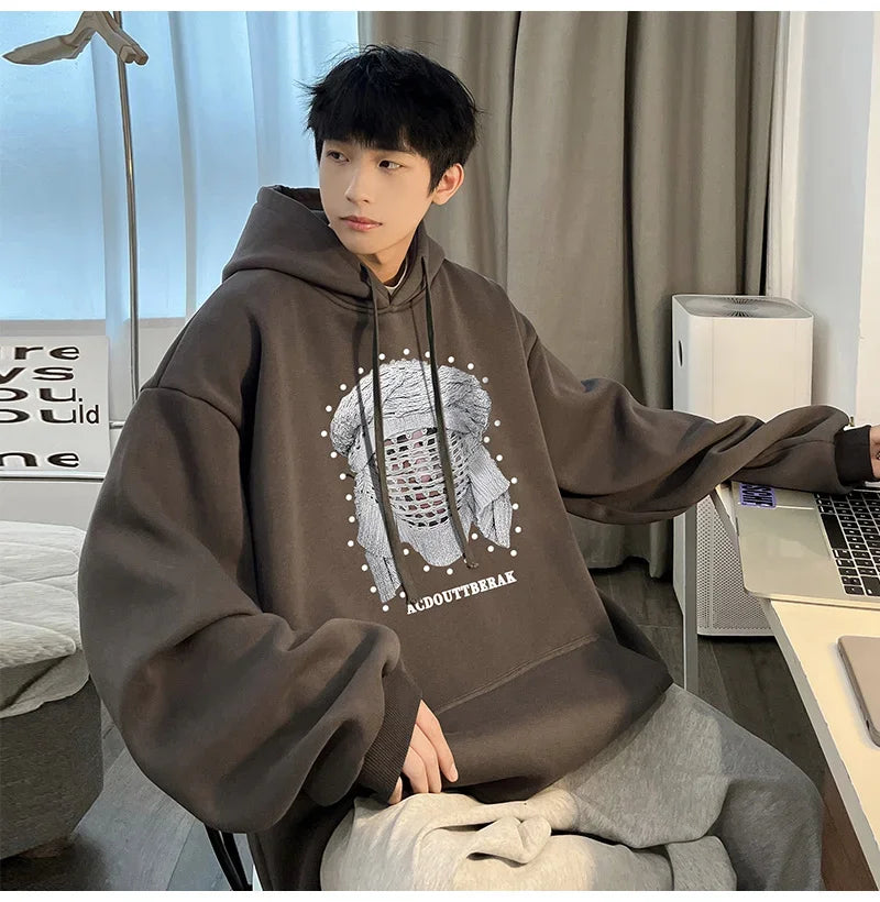 VOIDWEAR VDR_SHDW_07 oversized goth hoodie with masked figure graphic, in black, styled in urban streetwear fit. Person wearing a brown hoodie with a graphic design, sitting in a room with a desk and computer.