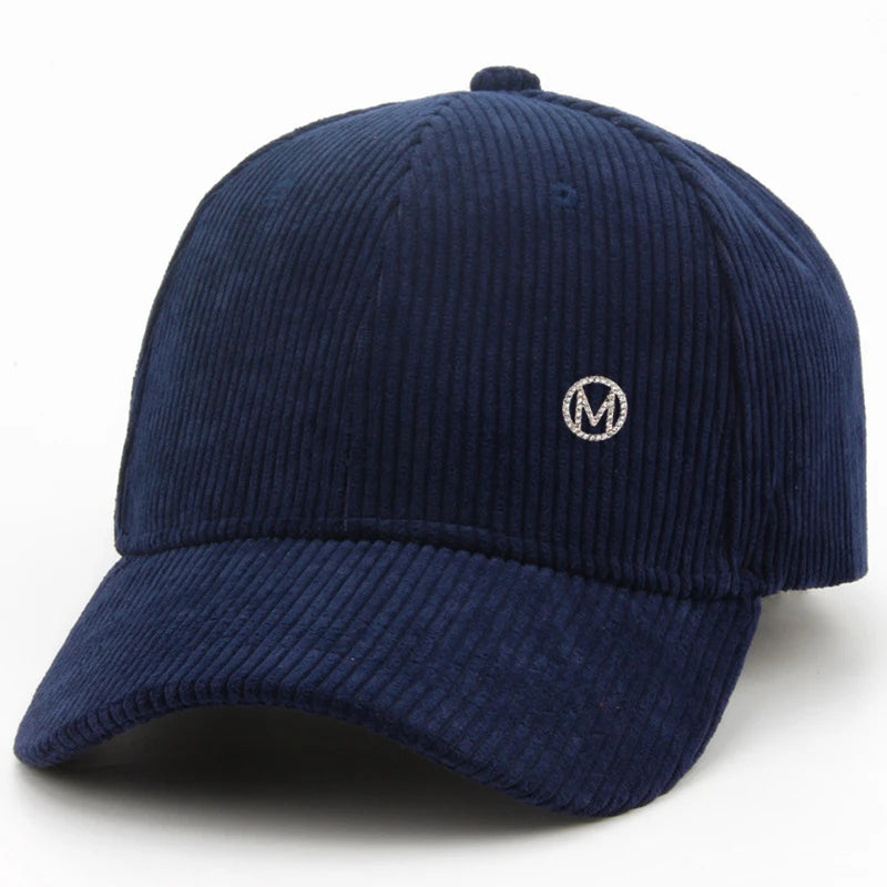 Diamond-studded M-letter corduroy baseball cap in solid color with adjustable strap, unisex streetwear headwear by VOIDWEAR.. Navy blue corduroy cap with a small white logo on a white background
