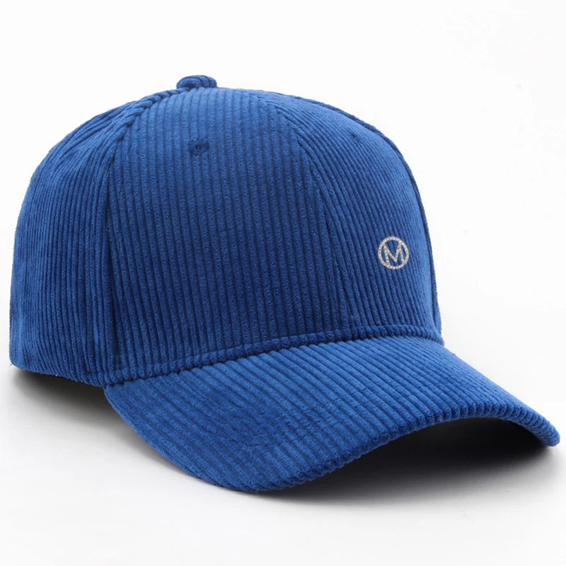 Diamond-studded M-letter corduroy baseball cap in solid color with adjustable strap, unisex streetwear headwear by VOIDWEAR.. Blue corduroy cap with a logo on a white background