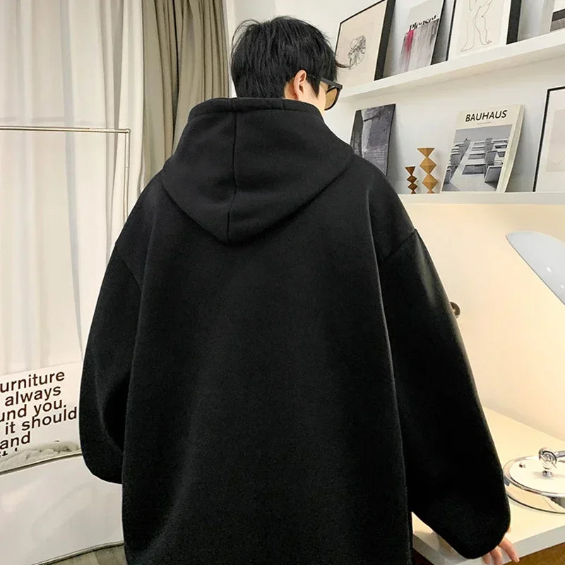 VOIDWEAR VDR_SHDW_07 oversized goth hoodie with masked figure graphic, in black, styled in urban streetwear fit. Person wearing a black hoodie in an indoor setting with a shelf and decor in the background.