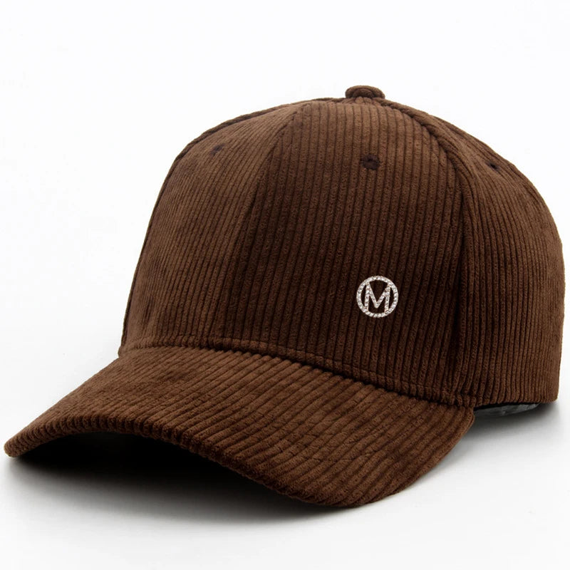 Diamond-studded M-letter corduroy baseball cap in solid color with adjustable strap, unisex streetwear headwear by VOIDWEAR. Brown corduroy cap with a logo on a white background