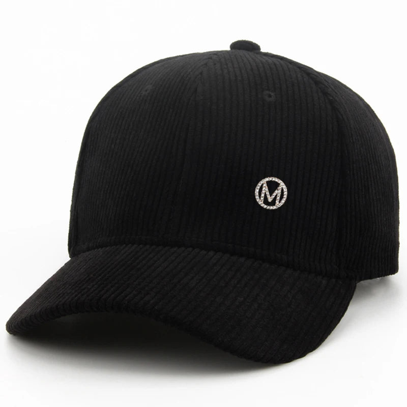 Diamond-studded M-letter corduroy baseball cap in solid color with adjustable strap, unisex streetwear headwear by VOIDWEAR.. Black corduroy cap with a white logo on a white background