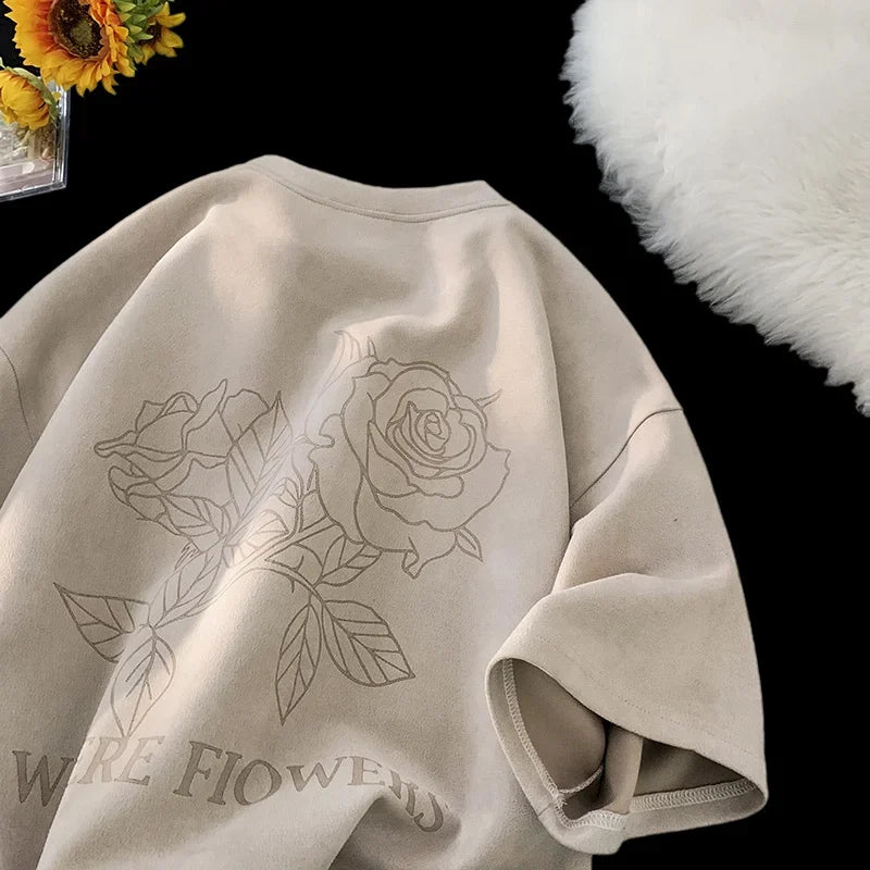 VOIDWEAR VDR_FLO_09 oversized goth floral graphic t-shirt in apricot, styled for streetwear layering. Beige sweatshirt with floral designs and text on a dark surface with flowers and a white fluffy object.