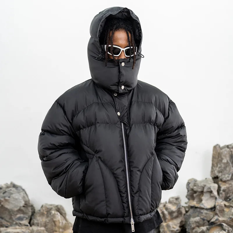 VOIDWEAR VDR_VANISH_05 ritual streetwear winter hooded jacket, oversized black coat with vanish-mode hood and signal glyph sleeve. Person wearing a black puffer jacket with a hood against a rocky background