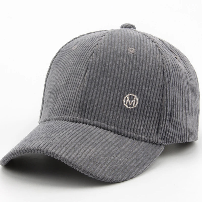 Diamond-studded M-letter corduroy baseball cap in solid color with adjustable strap, unisex streetwear headwear by VOIDWEAR.. Gray corduroy cap with a logo on a white background