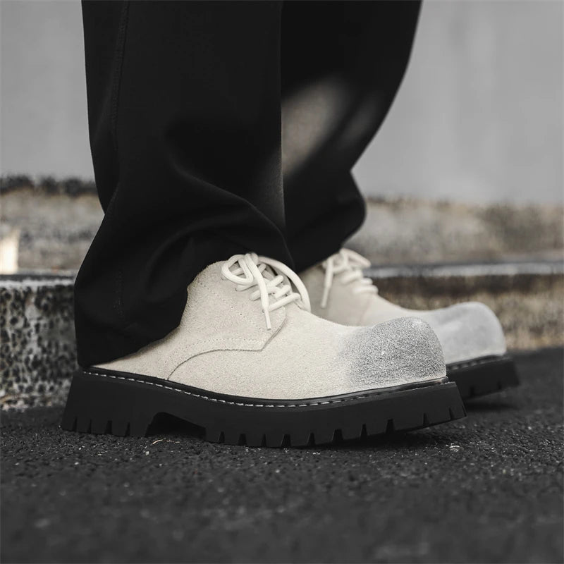 Men’s VOIDWEAR VDR_SIGNAL_03 derby shoes in black leather with thick rubber sole, slip-on design, and ritual-inspired streetwear aesthetic. Gray suede shoes with black soles worn by a person on a concrete surface.