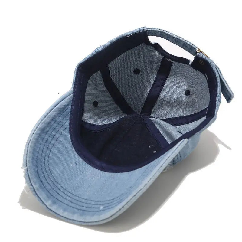 Vintage washed denim snapback by VOIDWEAR with distressed holes, ritual glyph detailing, and adjustable strap, designed for all-season streetwear.. Blue denim cap with navy interior on a white background