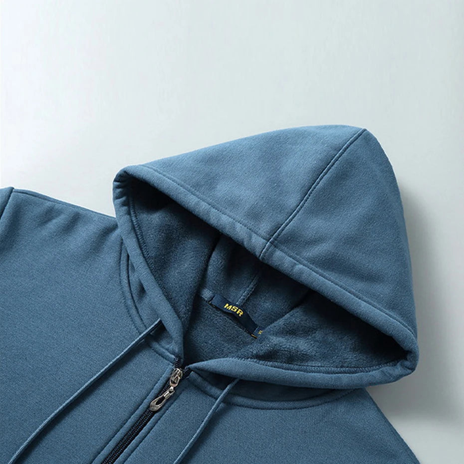 Blue hoodie with a zipper on a light gray background. OIDWEAR SHADOW_SYSTEM_07 ☰ full-zip hoodie shown worn in a concrete alleyway in winter, highlighting the oversized fit and fleece material.